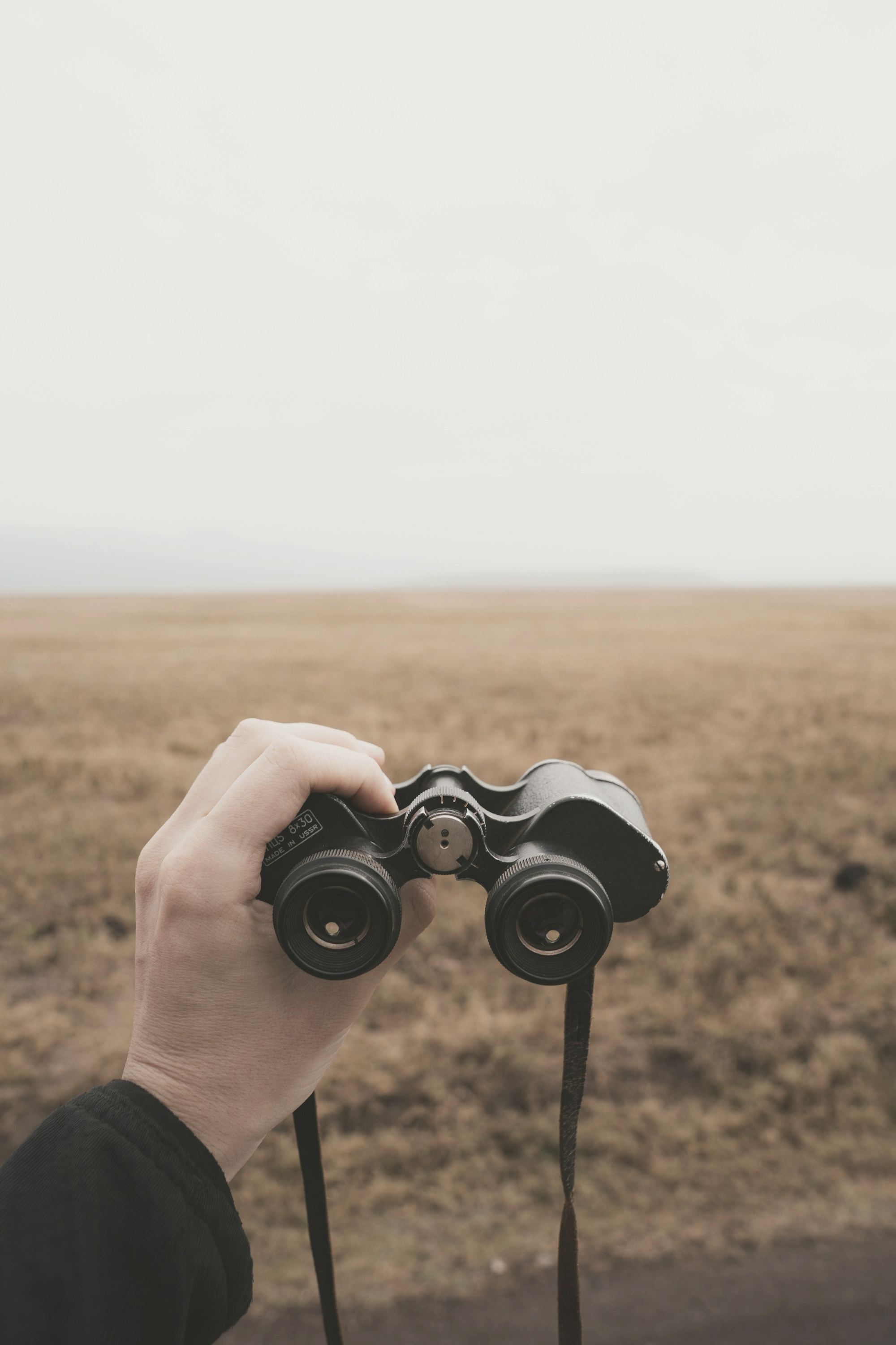 A hand holding binoculars over an open landscape